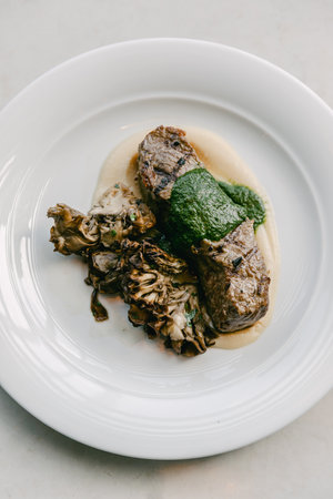 A beautifully plated beef dish with herb sauce and sautの写真素材