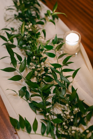 A table is adorned with lush greenery and small white flowers alongside a flickering candle, creating a cozy atmosphere.の写真素材