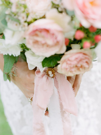 Bride gracefully holds a beautiful bouquet adorned with soft pink and white flowers, tied with a delicate ribbon.の写真素材