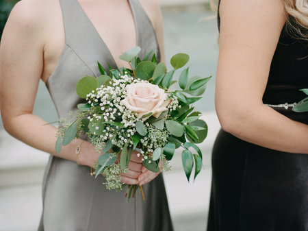 A bridesmaid stands gracefully with a fresh bouquet of pink roses at a lovely outdoor wedding.の写真素材