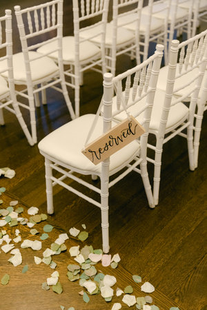 White chairs are reserved for guests at a wedding, surrounded by delicate flower petals on a wooden floor.の写真素材
