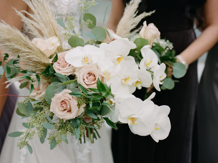Bridesmaids present a stunning floral arrangement featuring orchids and roses at a garden wedding.の写真素材