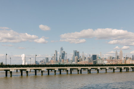 A large sculpture stands on a pier while modern buildings rise in the background under a partly cloudy sky.の写真素材