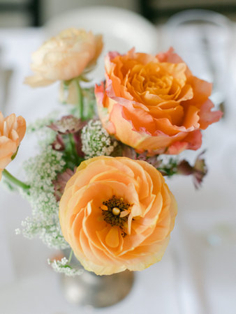 Beautiful orange and yellow roses with delicate greenery brighten a dining table at a celebratory gathering.の写真素材