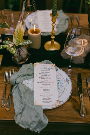 A beautifully arranged dinner table features an elegant place setting with floral china, a lit...