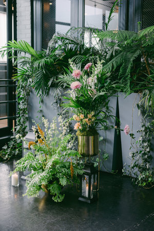 A vibrant display of flowers in a metallic vase stands amidst tropical plants in a stylish indoor area. The soft lighting creates a calm and inviting atmosphere, perfect for relaxation.の写真素材