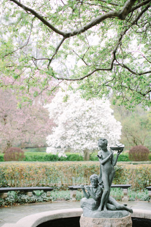 A beautiful sculpture of children playing flutes surrounded by lush greenery and blossoming trees in springtime.の写真素材
