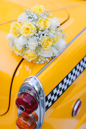 A lovely bouquet of yellow and white roses rests on a bright yellow taxi, showcasing urban charm.の写真素材