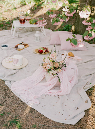 Elegant spring picnic under blooming cherry trees with delicious treats and floral arrangements