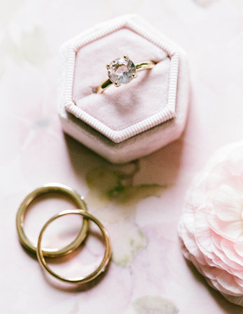 Elegant engagement ring and wedding bands displayed on soft surface with flower accents for romantic settingの写真素材