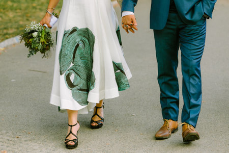 Couple walks hand in hand on a park path, dressed in formal attire, enjoying a romantic moment together.の写真素材