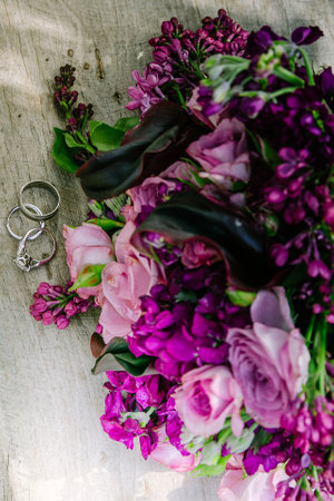 Wedding rings rest on a wooden table beside a vibrant bouquet of purple and pink flowers symbolizing love and joy.の写真素材