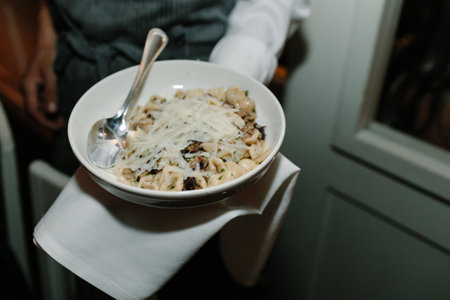 A waiter presents a bowl of creamy pasta topped with cheese in a cozy restaurant setting at night.の写真素材