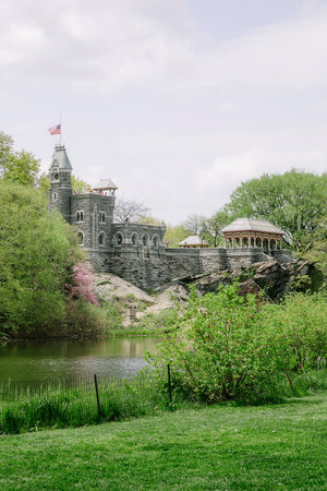 A charming stone castle overlooks a serene pond, framed by lush trees and blooming flowers on a clear spring day.の写真素材