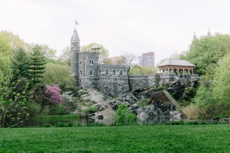 A picturesque view showcases a castle-like structure and gazebo amidst lush greenery and a serene pond in a busy city.の写真素材