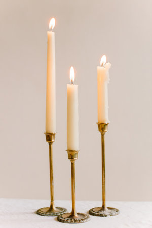 Three tall white candles burn brightly on ornate brass candle holders, creating a warm and inviting ambiance.の写真素材