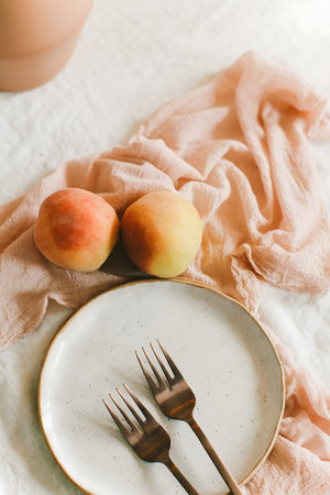 A simple setup features ripe peaches on a delicate linen, a white plate with two elegant forks, ideal for summer dining.の写真素材