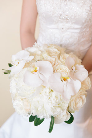 Bride holds a stunning bouquet of white flowers, including orchids and roses, while preparing for the wedding ceremony.の写真素材