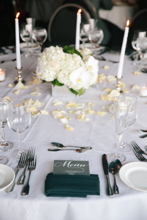 An elegant dinner table set with candles, flower centerpieces, and refined tableware.の写真素材