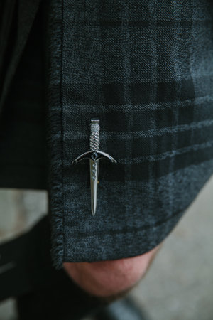 A silver sword brooch on a plaid blazer adds style at an outdoor gathering.