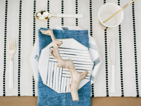 Dining table arranged with an octagonal plate, linen, and a decorative branch for an elegant, modern touch.の写真素材