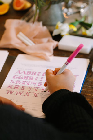 A hand carefully traces letters in calligraphy during a workshop, surrounded by decorative elements and snacks.の写真素材