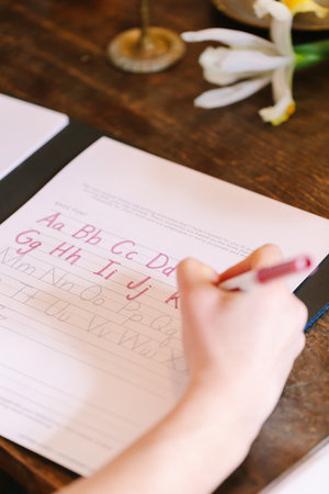A person practices handwriting in a notebook, surrounded by colorful flowers in a cozy setting.の写真素材
