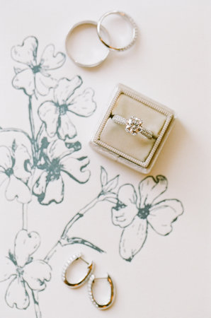 Beautiful engagement ring and earrings displayed on delicate floral artwork, perfect for a romantic celebration.の写真素材