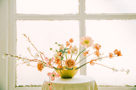 A beautiful arrangement of blossoms in soft hues adorns a simple table near a sunlit window.