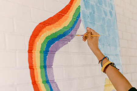 A hand paints vibrant colors of a rainbow design on a white brick wall in a bright workspace.の写真素材