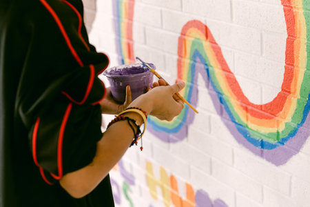 Artist applies turquoise paint to a lively mural featuring a rainbow while working in an artistic environment.の写真素材
