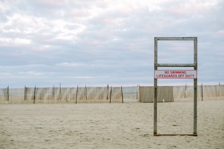 A lone lifeguard sign stands on quiet sand under a cloudy dusk sky, creating a serene atmosphere.の写真素材
