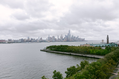 Cloudy skies loom over the waterfront with lush greenery and the distant city skyline reflecting a...