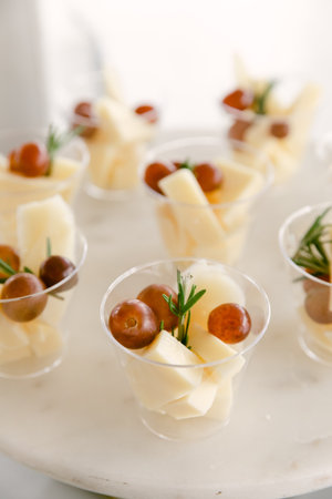 Five clear cups filled with fresh grapes and cheese are arranged on a marble surface.の写真素材