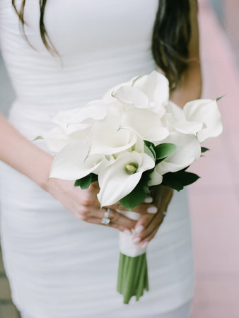 A bride carries a stunning bouquet of white calla lilies, preparing for her wedding day in a vibrant setting.の写真素材