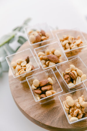 Bowls of mixed nuts arranged neatly on a wooden tray for social nibbling during an event or gathering.の写真素材