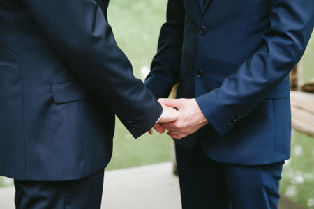 Two men hold hands in celebration of their wedding vows in a serene outdoor setting, surrounded by nature.の写真素材