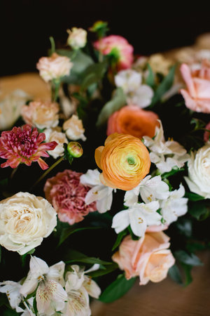 A vibrant flower arrangement highlights ranunculus, roses, and lilies on a wooden surface in a cozy...