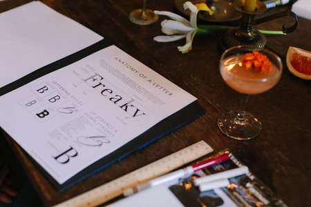 A unique workspace features a menu on letter design and a cocktail, showcasing creativity and...