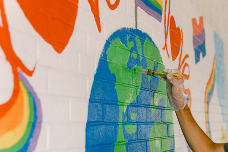 A person applies green paint to a mural of the Earth on a brick wall, surrounded by bright colors and shapes.の写真素材