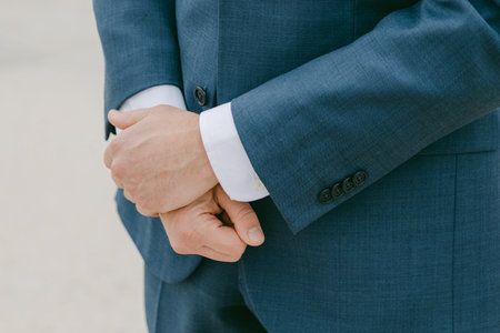 A man stands in a tailored suit, hands clasped, ready for an important event outdoors, capturing...