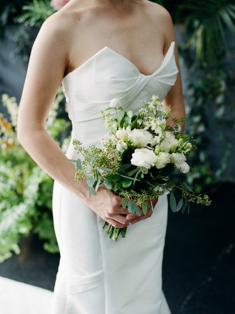 A bride stands gracefully, clutching a beautiful bouquet as she prepares for her outdoor wedding celebration.の写真素材