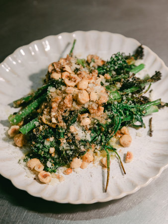 Fresh broccolini topped with crushed hazelnuts and flavorful breadcrumbs on a rustic white plate.の写真素材