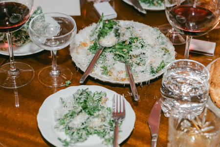 Guests enjoy delicious salads topped with cheese, paired with fine wine, creating an elegant dining atmosphere at night.の写真素材