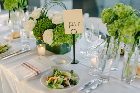 Tablescape features green flowers, a fresh salad, and elegant glassware, creating a sophisticated...