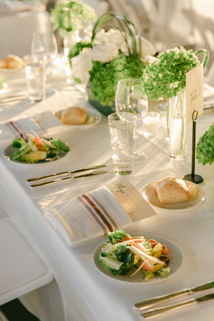 Guests enjoy a beautifully arranged table with fresh salads, bread rolls, and floral decorations during a daytime event.の写真素材