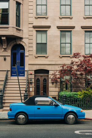 A vibrant blue convertible is parked beside a charming brownstone building with lush greenery nearby.の写真素材