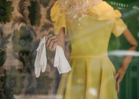 A mannequin displays a yellow dress and holds white gloves in a boutique window on a bright day.の写真素材
