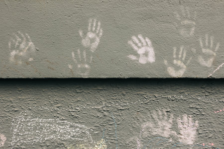 Colorful handprints in chalk adorn a weathered gray wall, reflecting community creativity and artistic expression.の写真素材