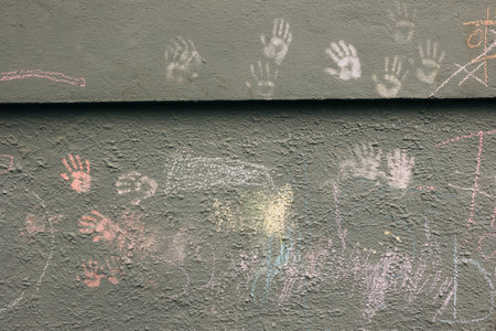 Children express themselves through colorful chalk drawings and handprints on a weathered wall in the playground.の写真素材